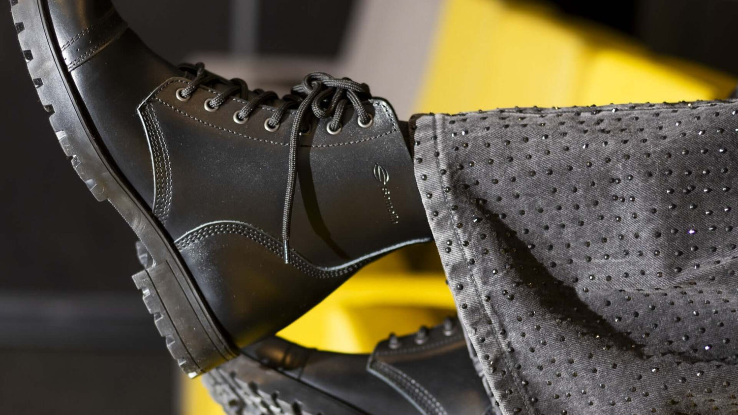 Close-up of stylish black men's boots paired with embellished grey pants, showcasing modern footwear fashion.