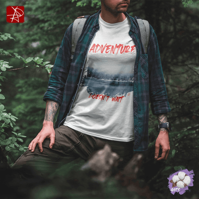 Unisex organic cotton t-shirt with 'Adventure Doesn't Wait' design over snowy lake scene, worn by a person in nature.