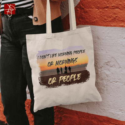Eco-friendly organic cotton tote bag with vibrant sunset design and humorous text about mornings and people.