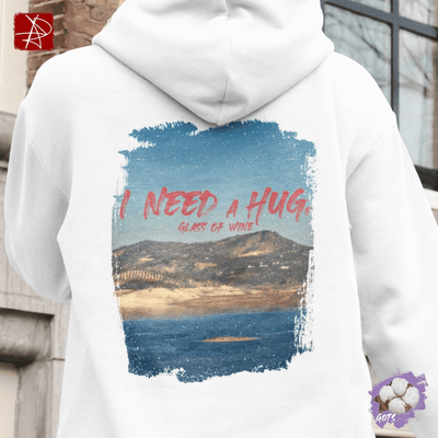 White hoodie featuring 'I Need A Huge Glass of Wine' with scenic lake background, perfect for wine lovers.