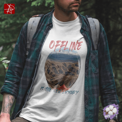 Man in organic cotton t-shirt with 'Offline is the New Luxury' design, standing in nature with mountains in background.